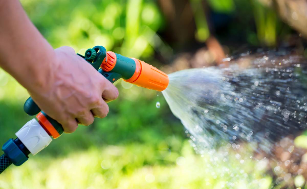 Man's hand holding a hose nozzle spraying water onto a lawn
