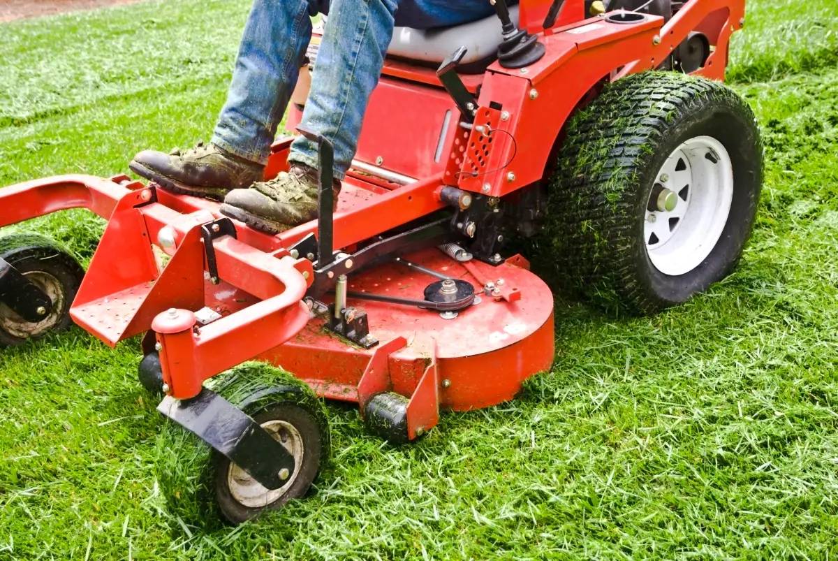 Man sitting on red riding lawnmower cutting the grass.