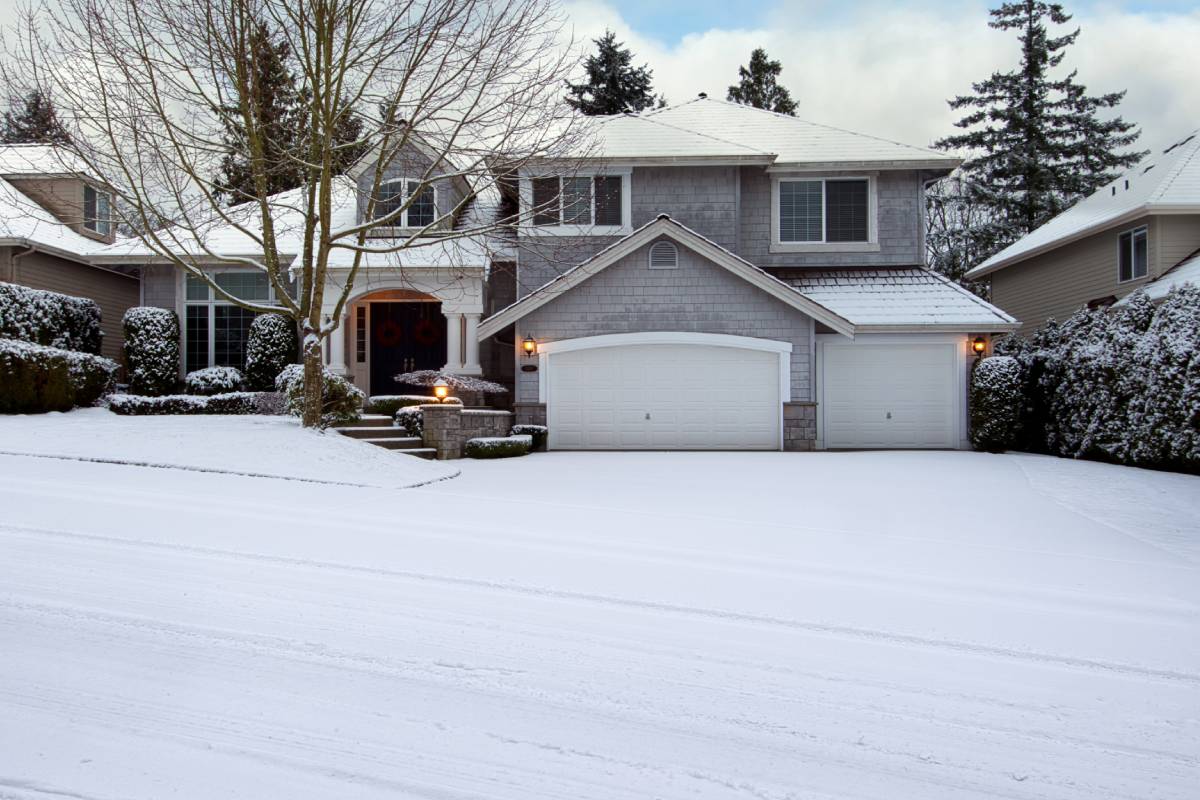 Large grey home with a driveway and front yard covered in snow.
